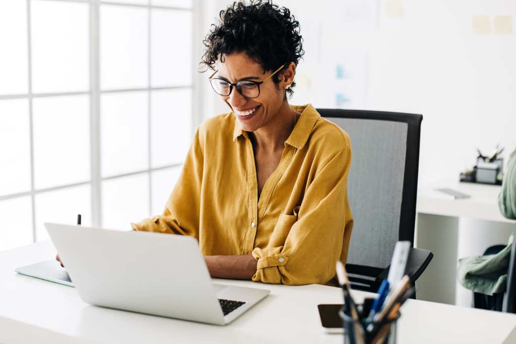 A woman smiles at her computer, representing satisfaction with her Learning Management System following best practices.