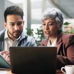 An older office worker and a younger Gen Z coworker examine product training.