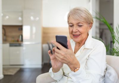 A senior woman smiles while using a smartphone at home, representing modern mobile-friendly online learning.